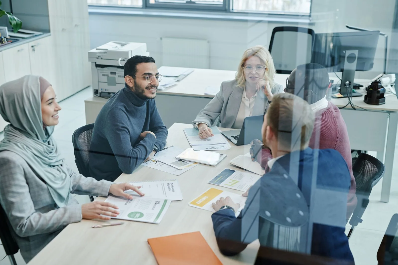 Ein diverses Team im Arbeitsgespräch an einem Konferenztisch in einem hellen Büro, Unterlagen vor sich.